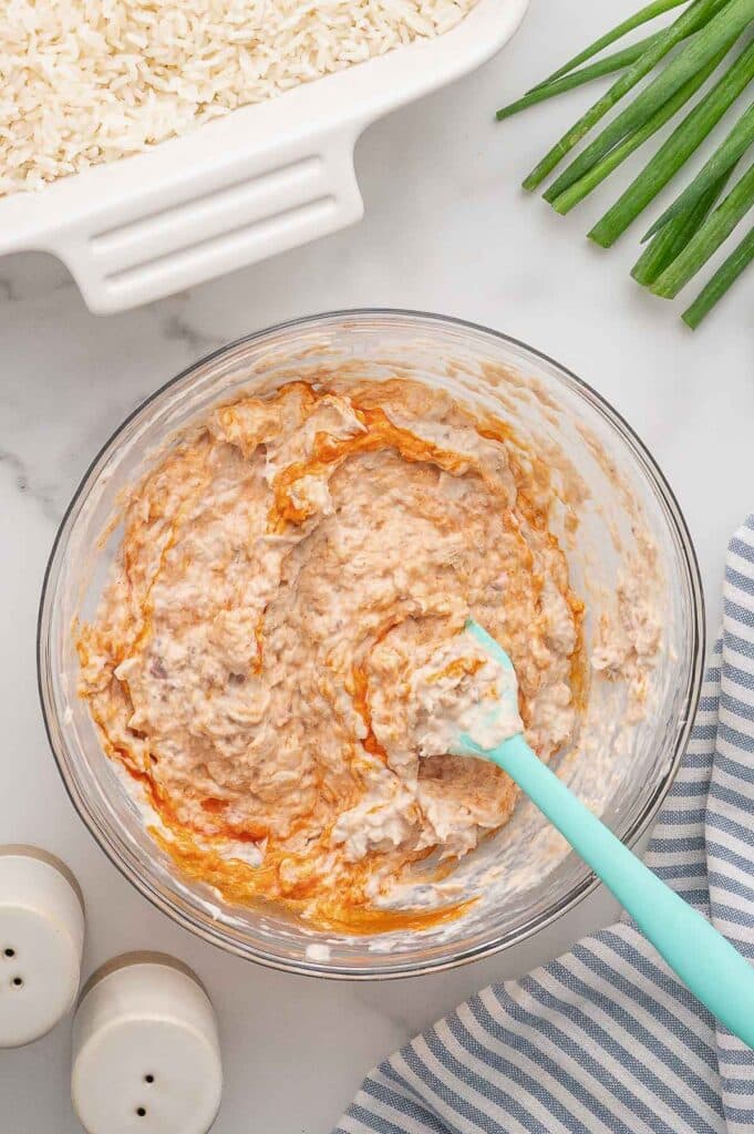 A glass bowl with a creamy spicy salmon mixture being stirred by a blue spatula.