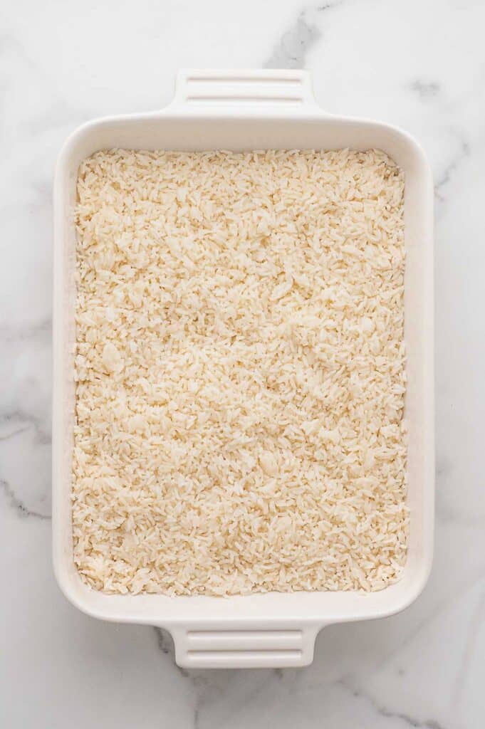 A white rectangular baking dish filled with rice along the bottom.