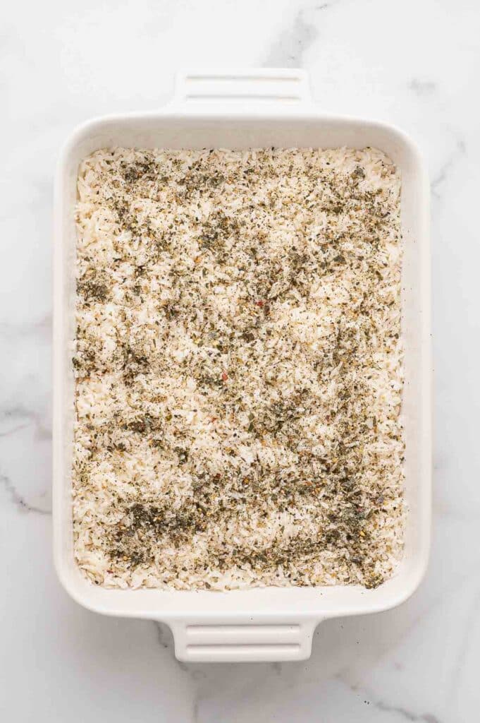 A white rectangular baking dish filled with uncooked white rice topped with furikake seasoning.