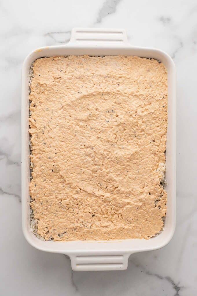 A white baking dish with a layer of rice and furikake seasoning topped with spicy salmon spread overtop.