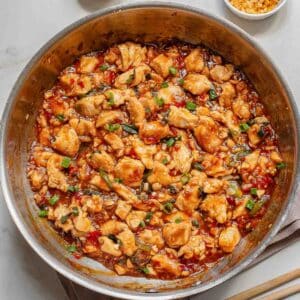A skillet filled with cooked diced chicken in a sweet chili sauce, garnished with green onions.