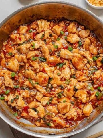 A skillet filled with cooked diced chicken in a sweet chili sauce, garnished with green onions.