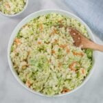 A bowl of creamy coleslaw with shredded cabbage and carrots, mixed with dressing, and a wooden spoon resting inside.