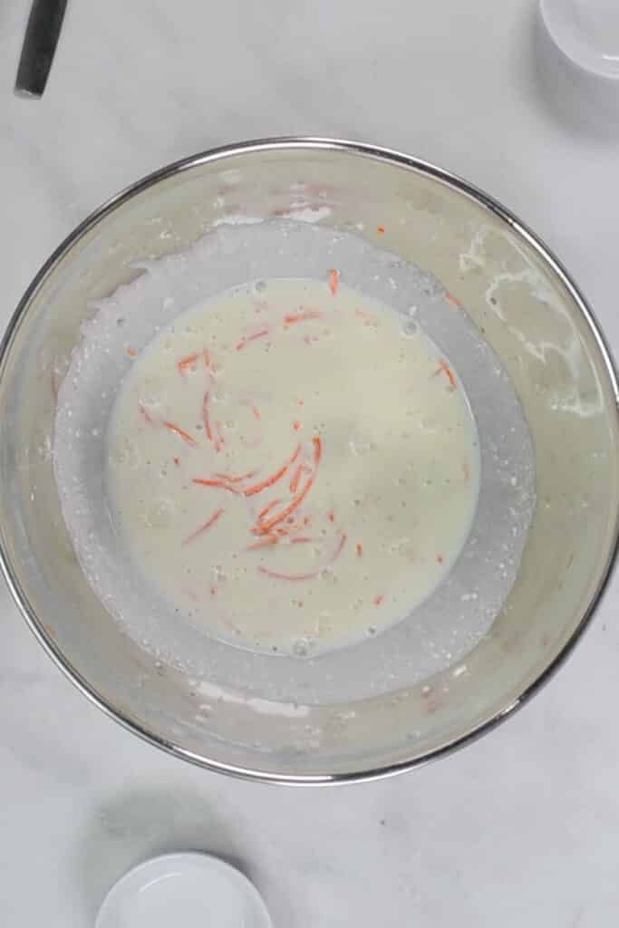 A stainless steel bowl containing a homemade coleslaw dressing mixture on a white countertop.