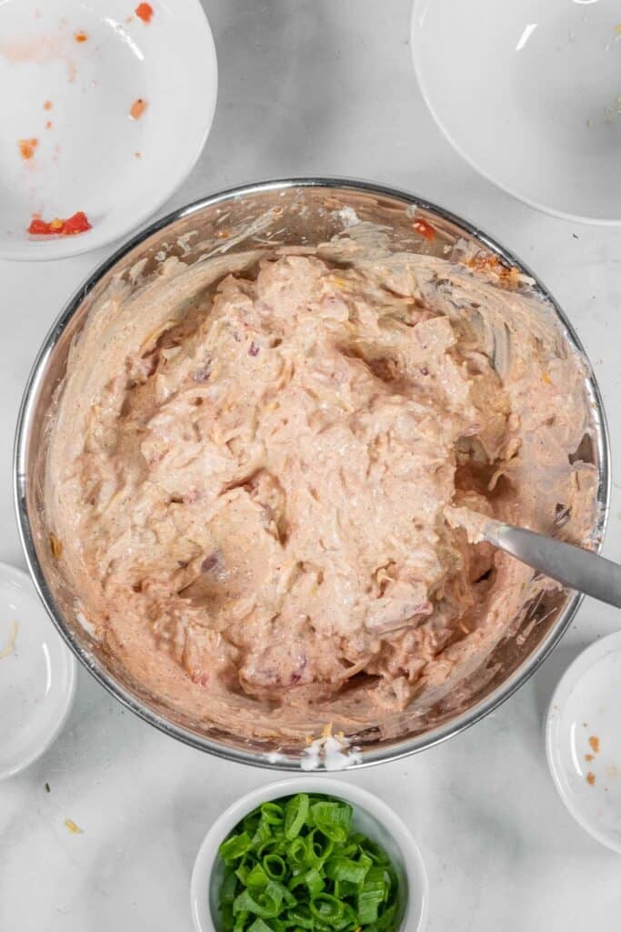 A metal mixing bowl filled with a creamy, chunky dip mixture containing all ingredients mixed together.
