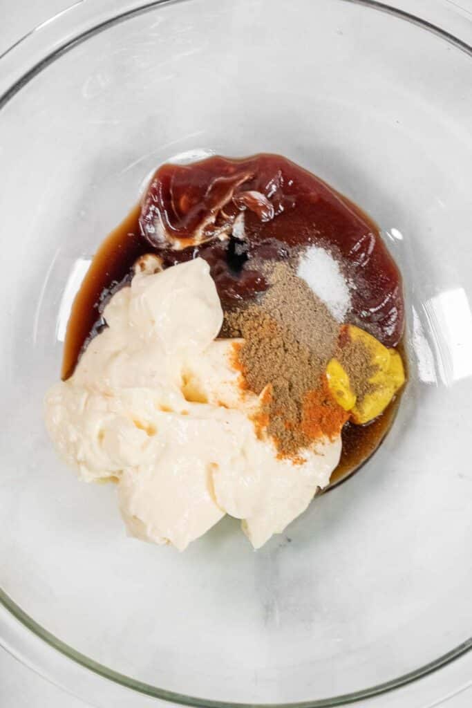 A glass bowl containing mayonnaise, ketchup, mustard, Worcestershire sauce, and various spices.