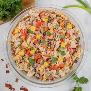 A clear glass bowl filled with cowboy pasta salad on a white surface.