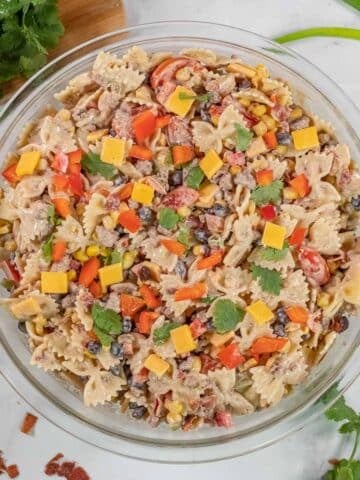 A clear glass bowl filled with cowboy pasta salad on a white surface.