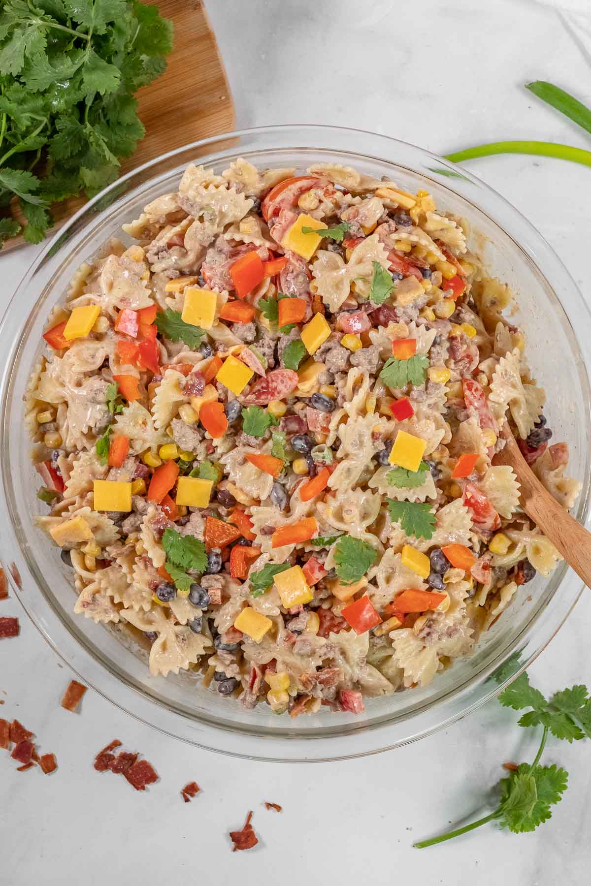 A clear glass bowl filled with cowboy pasta salad on a white surface.