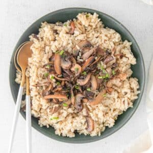 A bowl filled with mushroom risotto garnished with chopped herbs, with golden spoons on the side.
