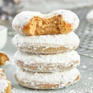 A stack of four powdered sugar donuts with a bite taken out of the top donut.
