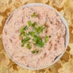 A bowl of viral boat dip recipe topped with chopped green onions, surrounded by tortilla chips on a white plate.