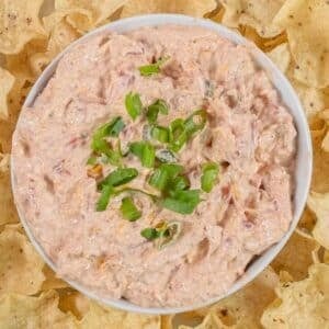 A bowl of viral boat dip recipe topped with chopped green onions, surrounded by tortilla chips on a white plate.