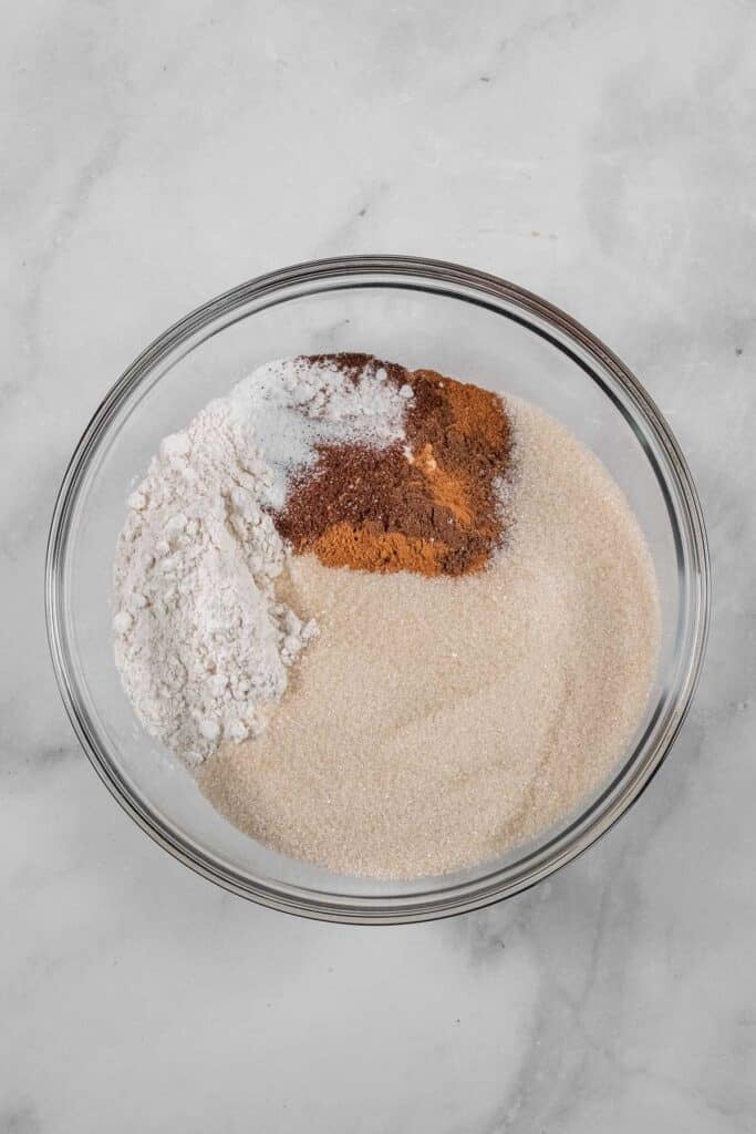 A glass bowl containing of flour, granulated sugar, cinnamon, cloves, allspice, salt, and baking powder.