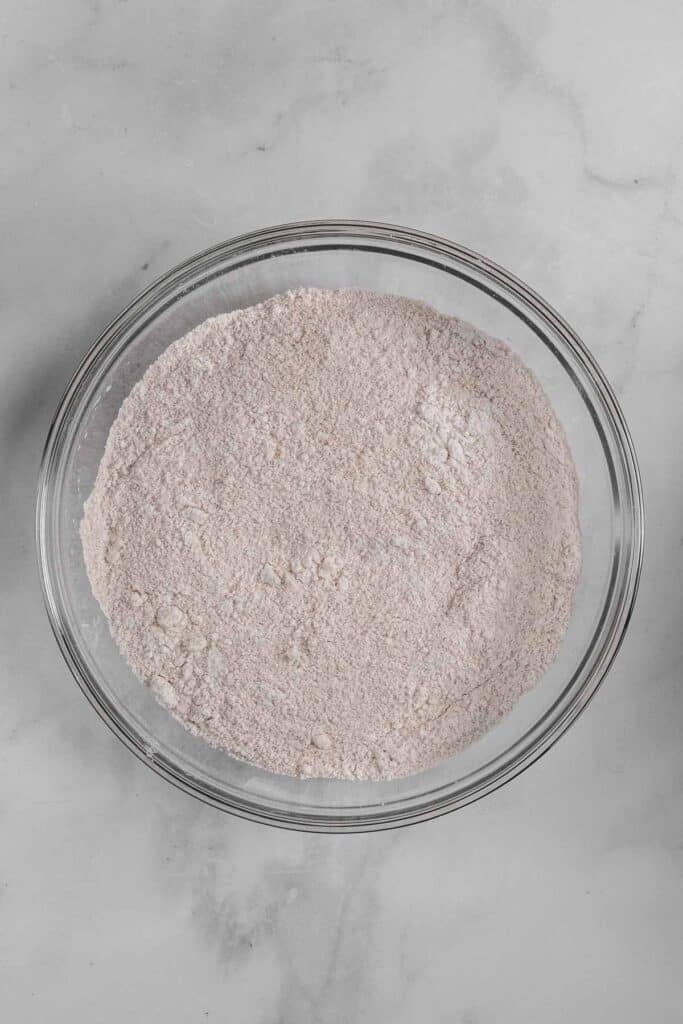 A glass bowl containing of flour, granulated sugar, cinnamon, cloves, allspice, salt, and baking powder mixed together.