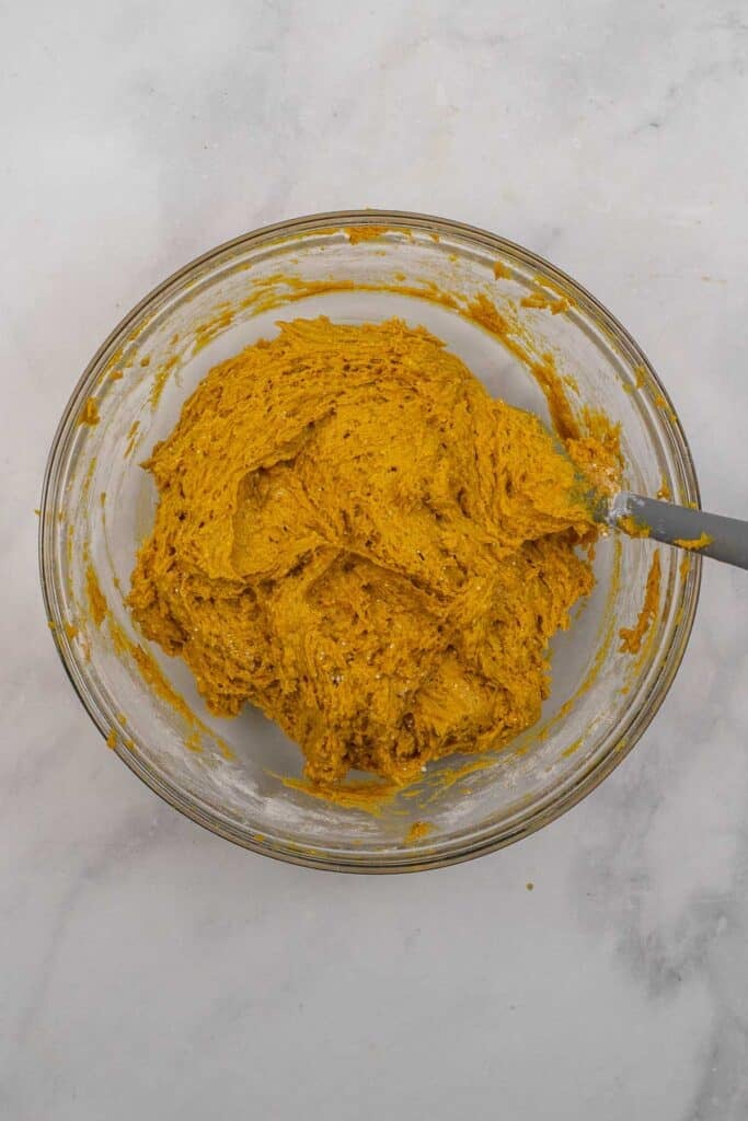A glass mixing bowl filled with pumpkin cake dough.