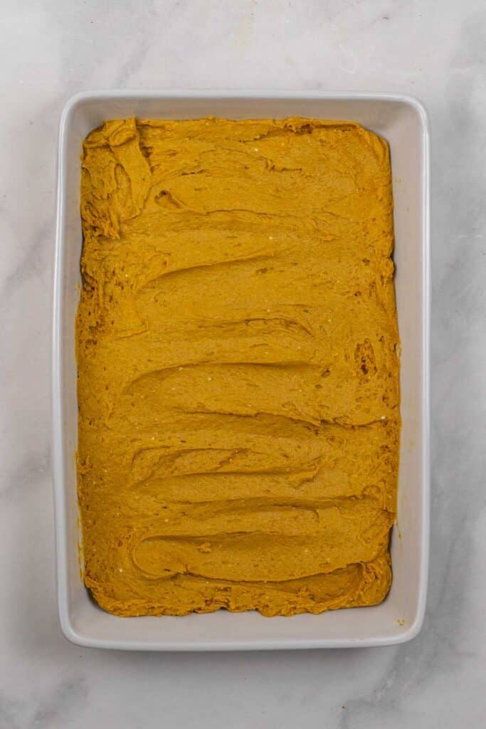 A rectangular baking dish filled with an even layer of unbaked pumpkin cake batter.