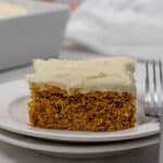 A slice of pumpkin cake with cream cheese frosting on a white plate, next to a fork.