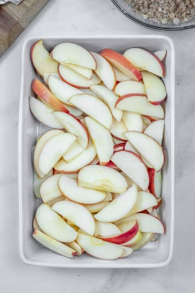 A rectangular white dish filled with sliced apples, arranged in overlapping layers on a marble surface.