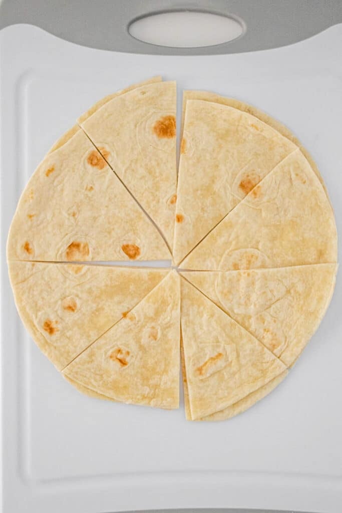A flour tortilla cut into eight triangular slices is displayed on a white cutting board.
