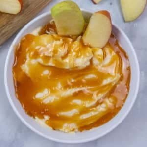 A bowl of creamy apple dip recipe topped with caramel sauce and garnished with two apple slices.