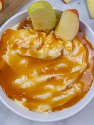 A bowl of creamy apple dip recipe topped with caramel sauce and garnished with two apple slices.