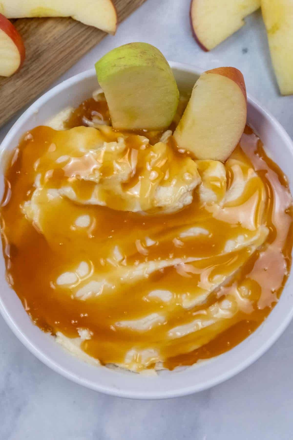 A bowl of creamy apple dip topped with caramel sauce, garnished with two apple slices.