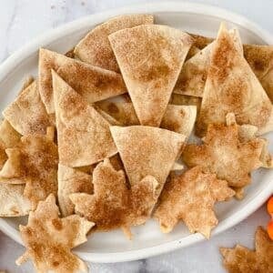 A plate of baked cinnamon tortilla chips shaped like triangles and maple leaves.
