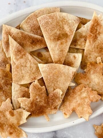A plate of baked cinnamon tortilla chips shaped like triangles and maple leaves.
