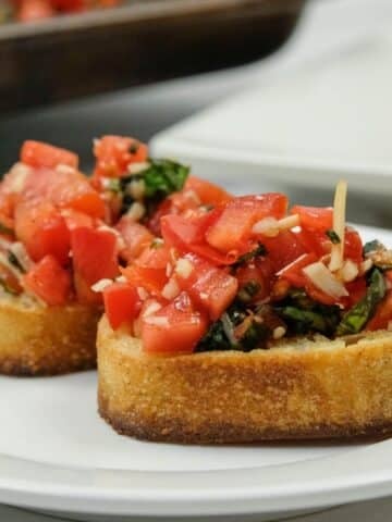 Two slices of toasted bread topped with a mixture of diced tomatoes, basil, garlic, and olive oil are served on a white plate.