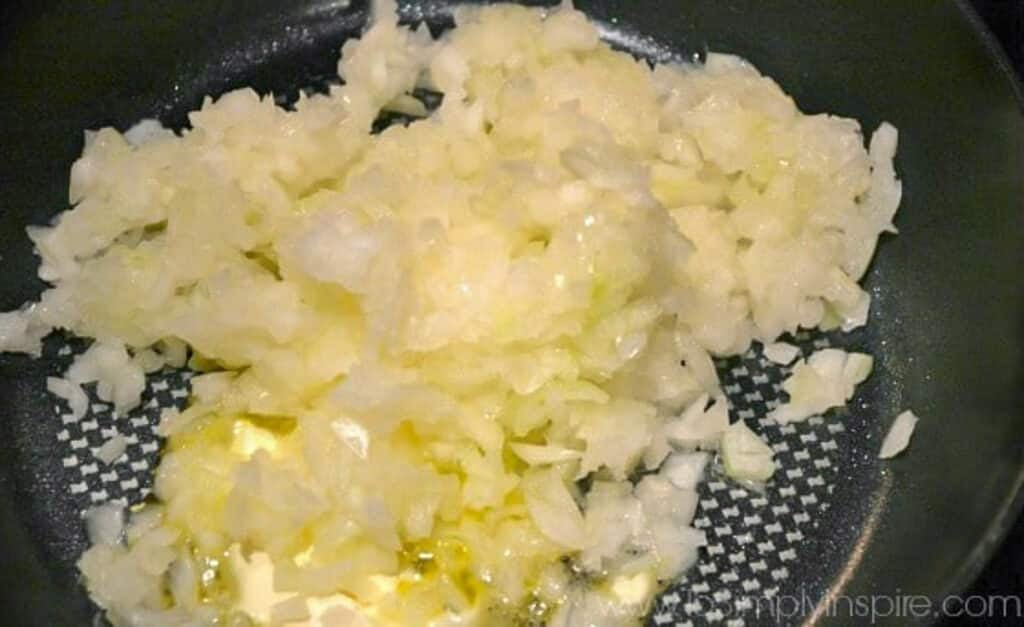 Chopped onions are being sautéed in butter in a frying pan.