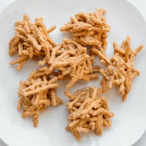 A white plate with a pile of no-bake haystacks made from chow mein noodles coated in a peanut butter butterscotch mixture.