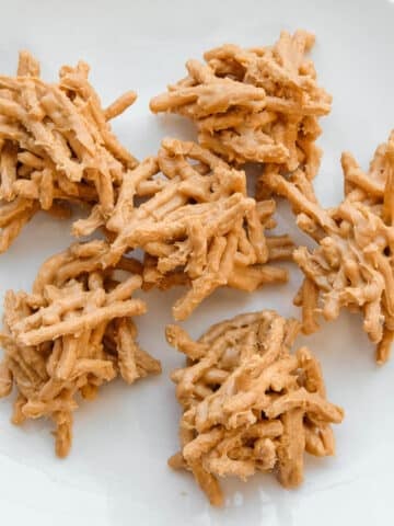 A white plate with a pile of no-bake haystacks made from chow mein noodles coated in a peanut butter butterscotch mixture.