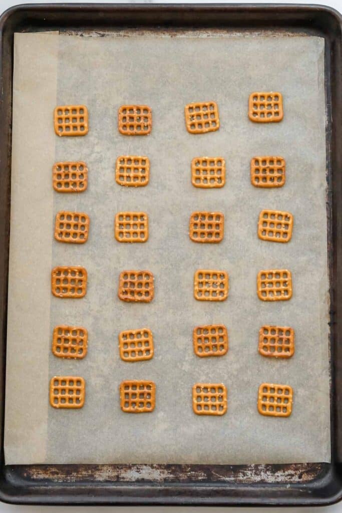 A baking sheet lined with parchment paper holds 20 square pretzels arranged in a grid pattern.