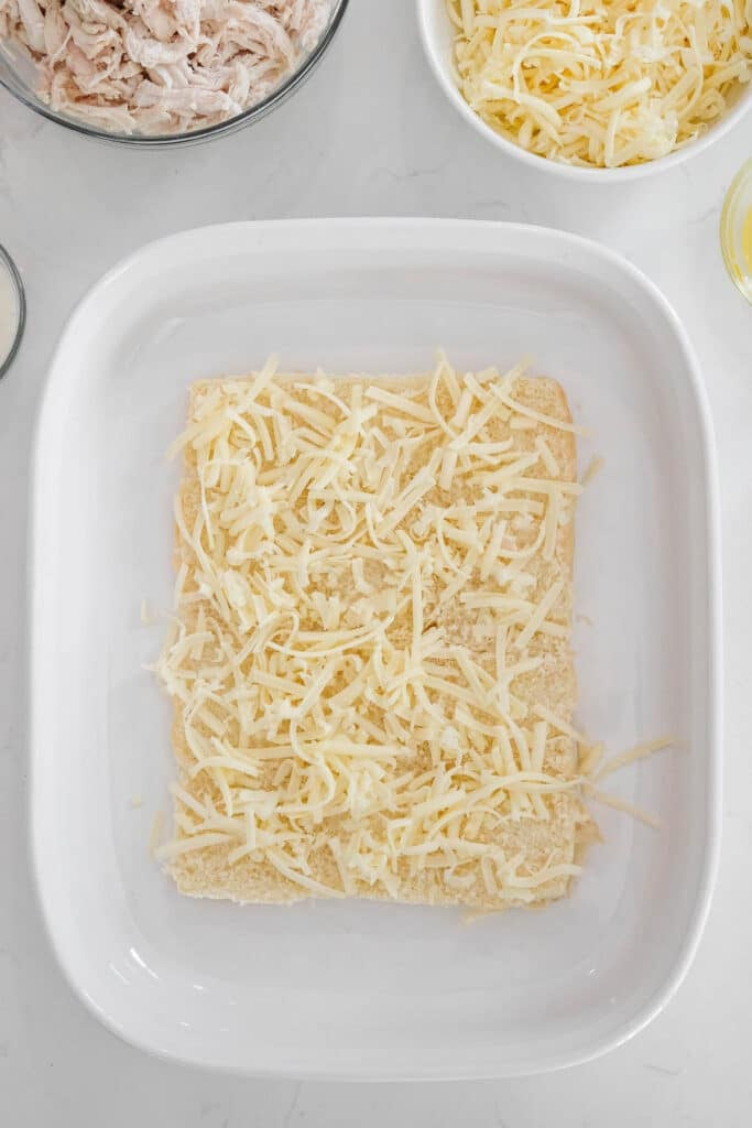 A white rectangle baking dish with the Hawaiian roll base of bread topped with shredded cheese.