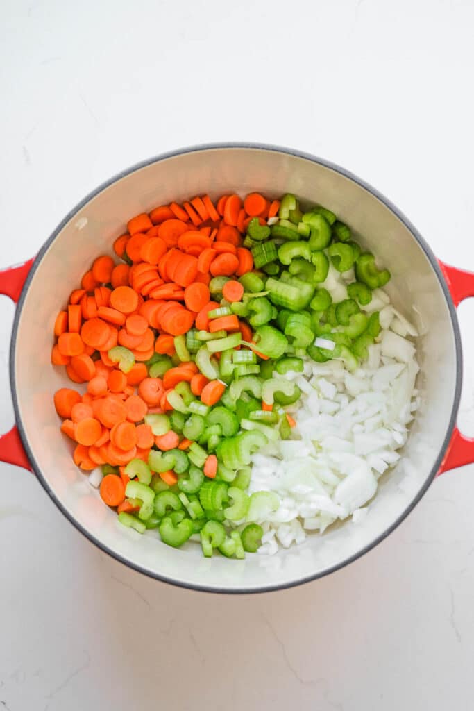 A pot containing chopped carrots, celery, and onions.