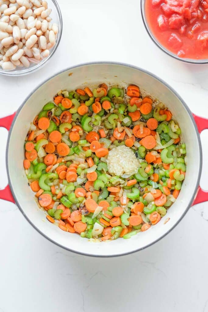A pot with sautéed carrots, celery, and onions, topped with minced garlic.