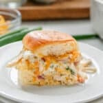 A close-up of a crack chicken slider served on a white plate, garnished with herbs.