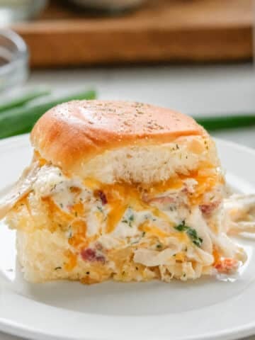 A close-up of a crack chicken slider served on a white plate, garnished with herbs.
