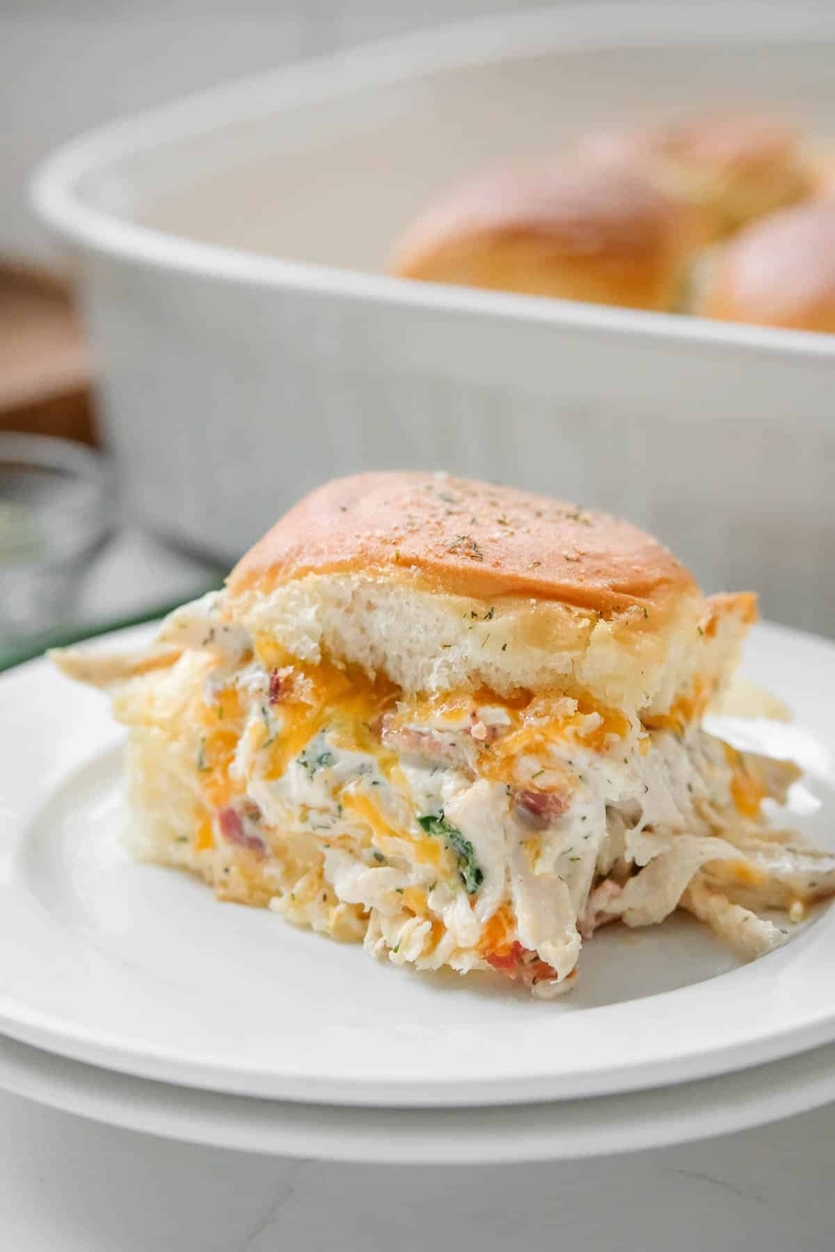 A close-up of a crack chicken slider served on a white plate, garnished with herbs.