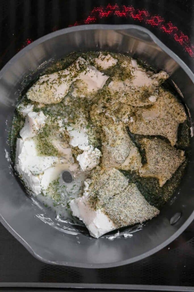 Cream cheese, seasonings, and herbs to be mixed together in a saucepan on a stovetop.