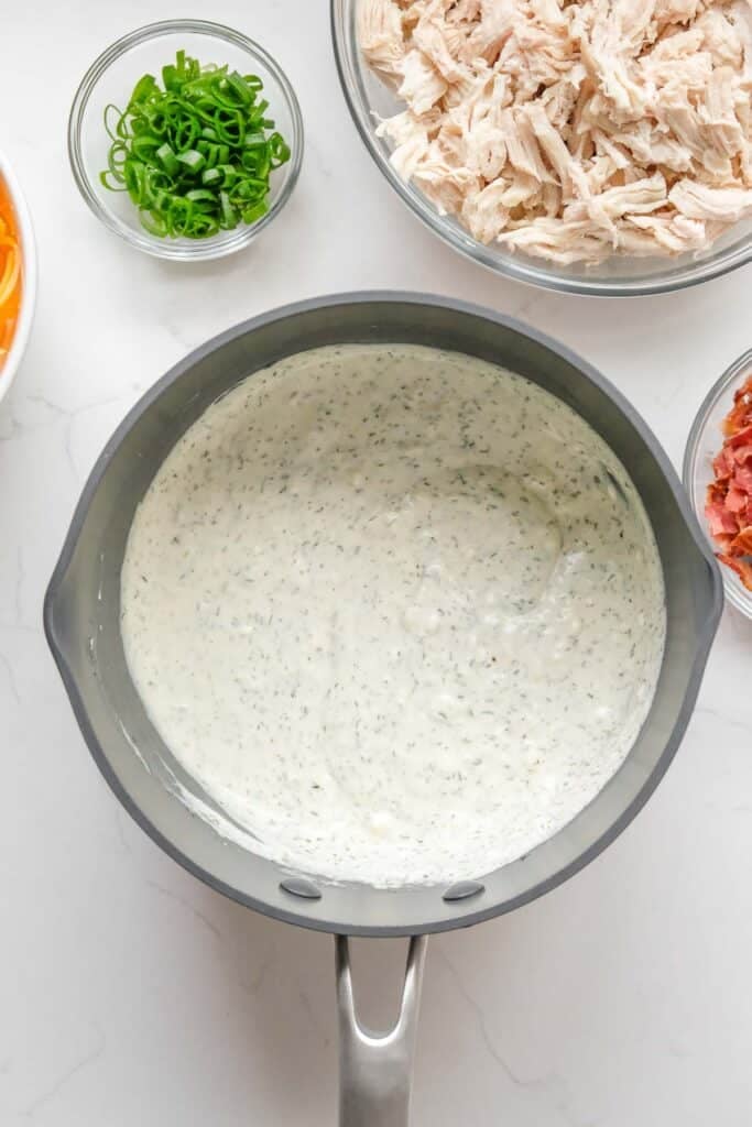 A saucepan of creamy sauce sits on a counter surrounded.
