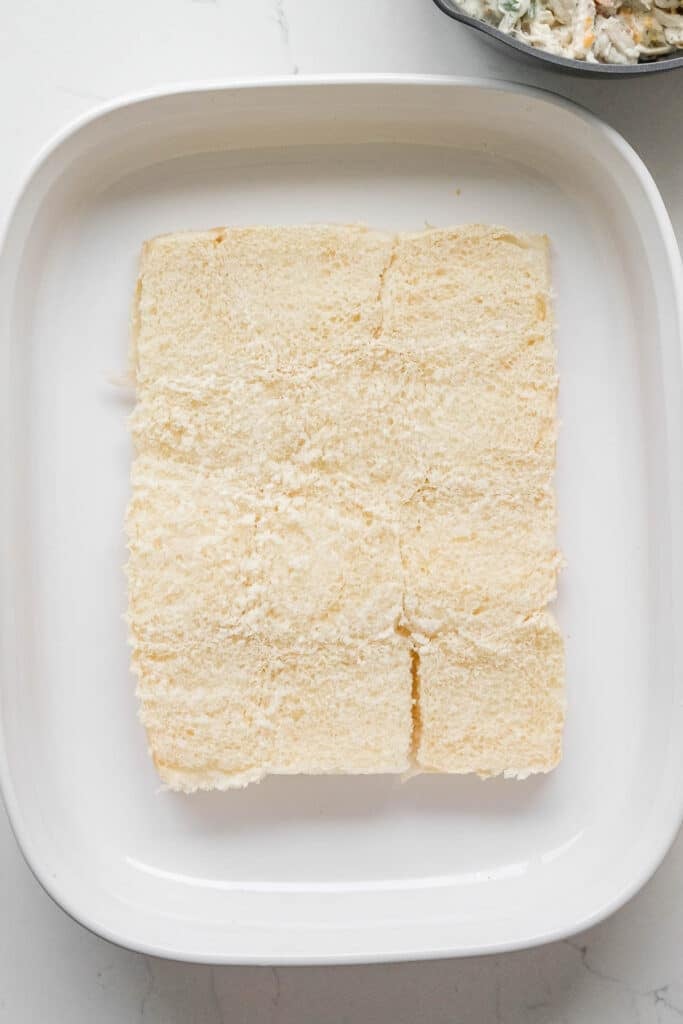 Bottoms of sliced Hawaiian rolls arranged to cover the bottom of a white rectangular baking dish.