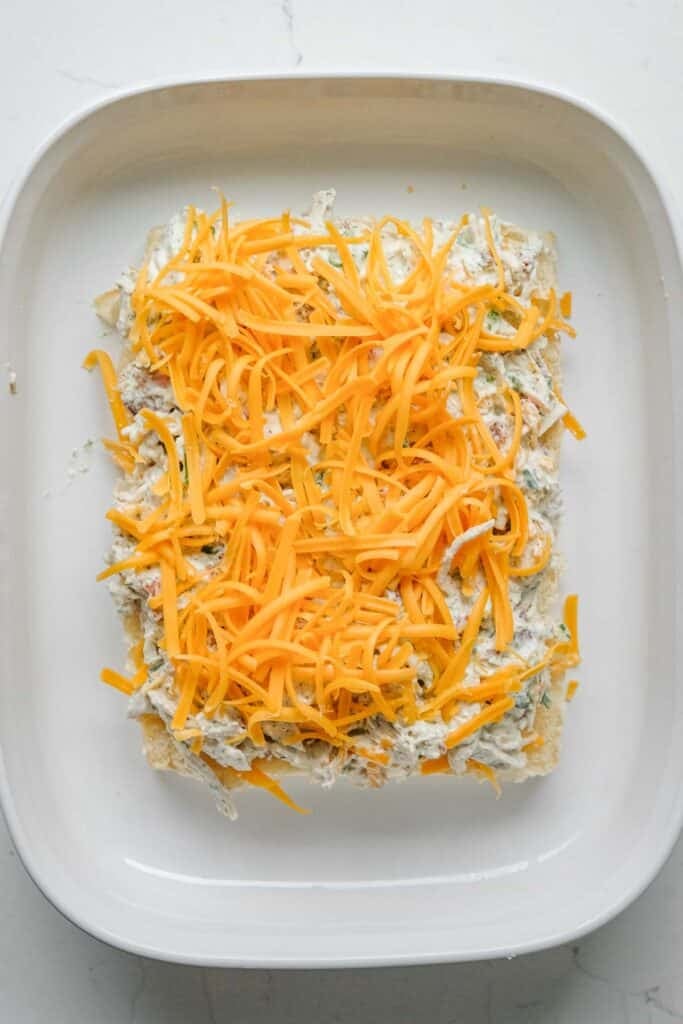 Casserole dish with a layer of creamy mixture topped with shredded cheddar cheese on top.