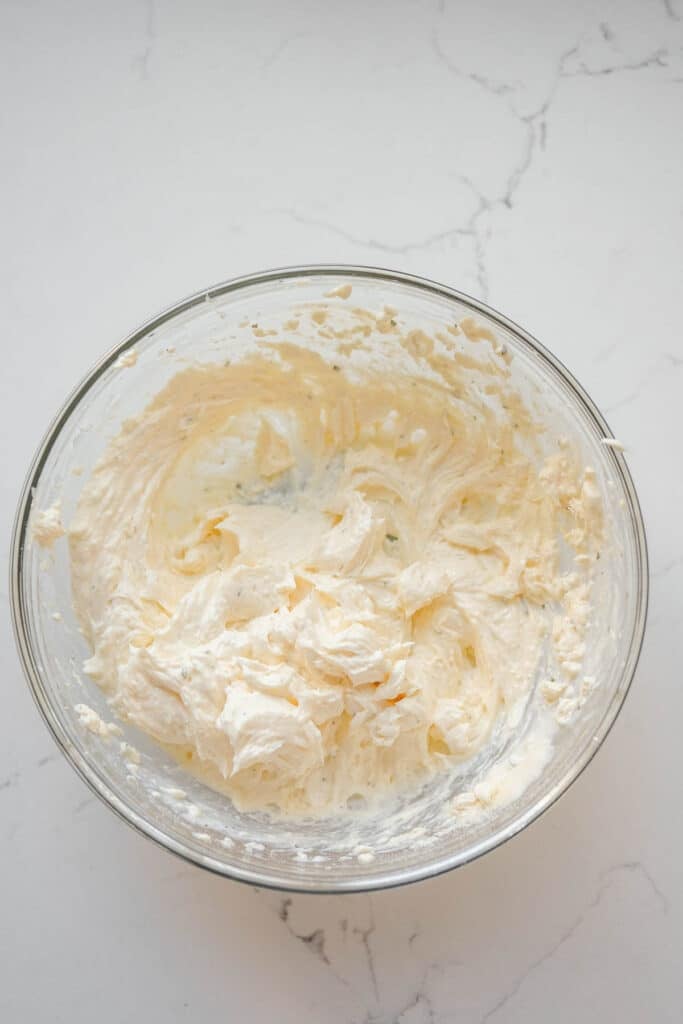 A glass bowl with cream cheese mixture on a white marble surface.