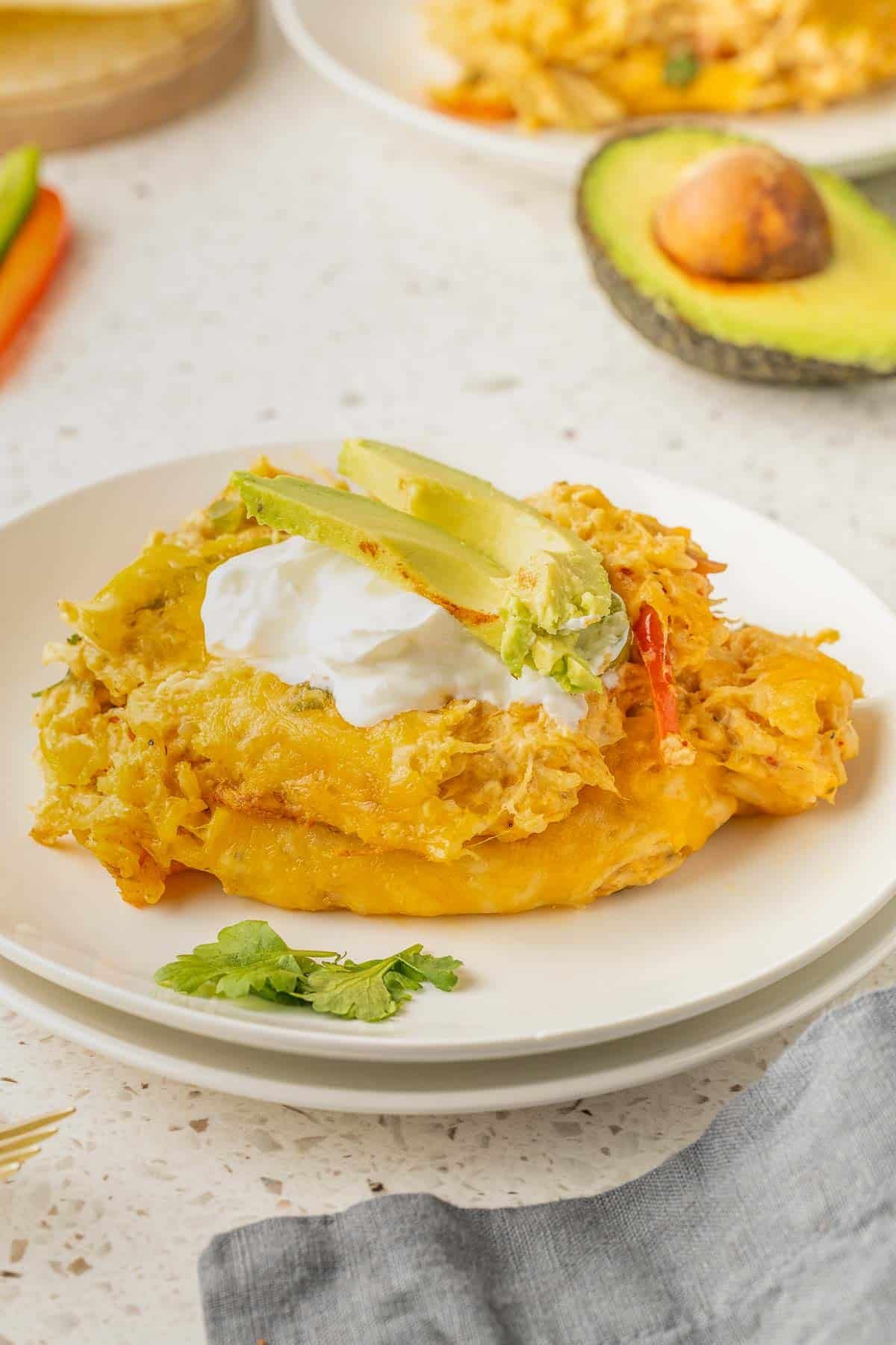 A plate with a serving of chicken fajita casserole topped with sour cream and avocado slices, garnished with cilantro.