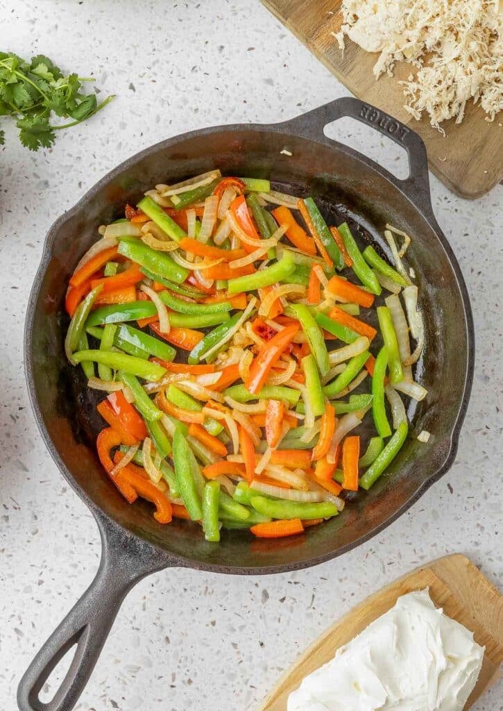 Sliced green beans, red bell peppers, and onions sautéing in a black cast iron skillet on a white countertop.
