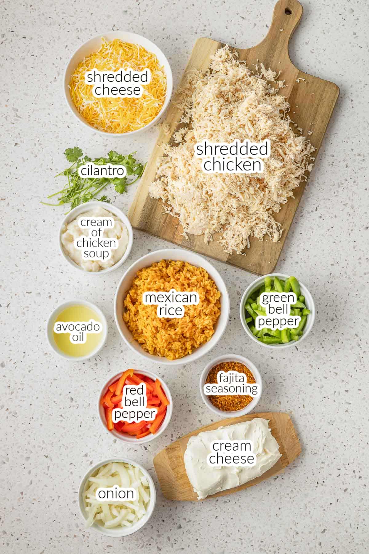 Ingredients for a Chicken Fajita Casserole are laid out on a counter, including shredded chicken, cheese, green and red bell peppers, mexican rice, avocado oil, cream of chicken soup, onions, cilantro and fajita seasoning.