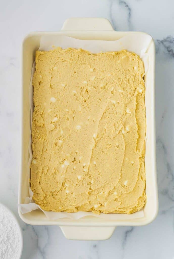 A rectangular baking dish lined with parchment paper filled with unbaked cookie dough, resting on a white marble surface.