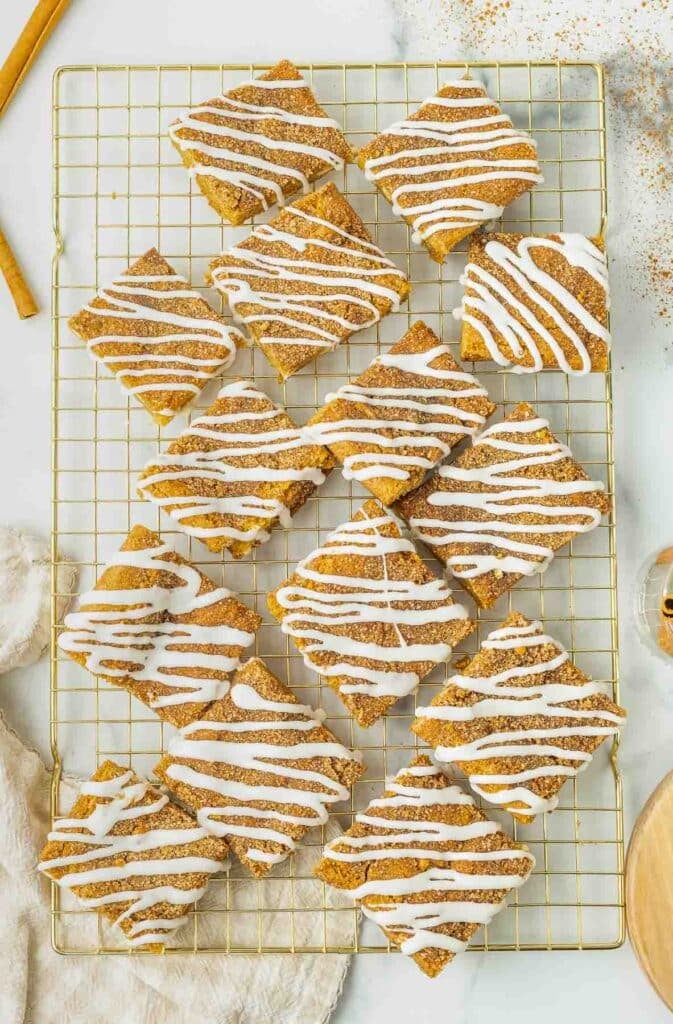 Twelve Snickerdoodle Cookie Bars with white icing drizzle arranged on a wire cooling rack, viewed from above.
